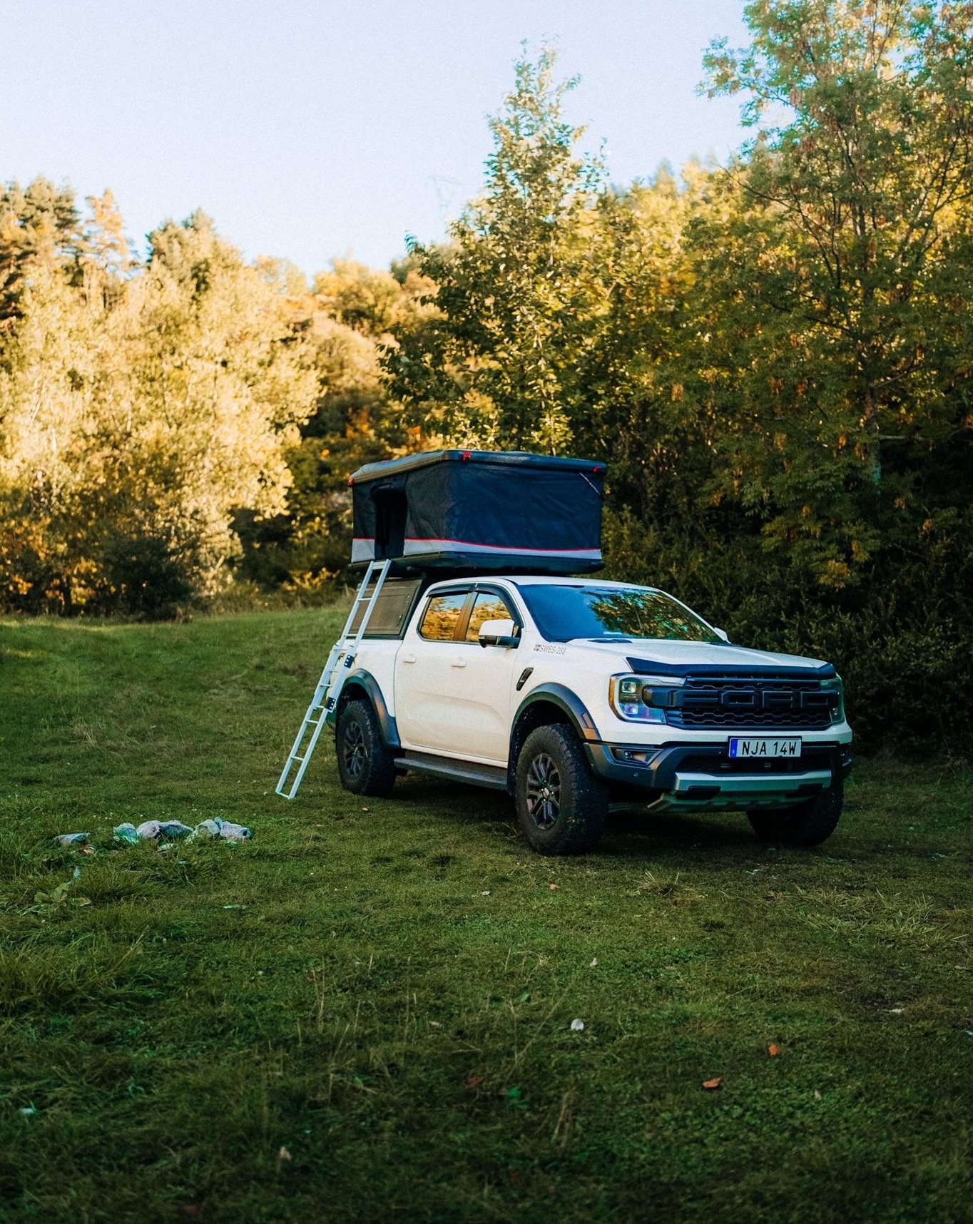 Ranger Raptor with rooftop tent at golden hour in a Nordic forest clearing